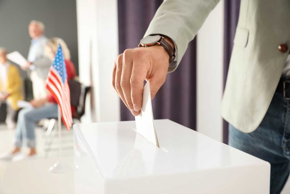 man putting ballot paper into box at polling stati